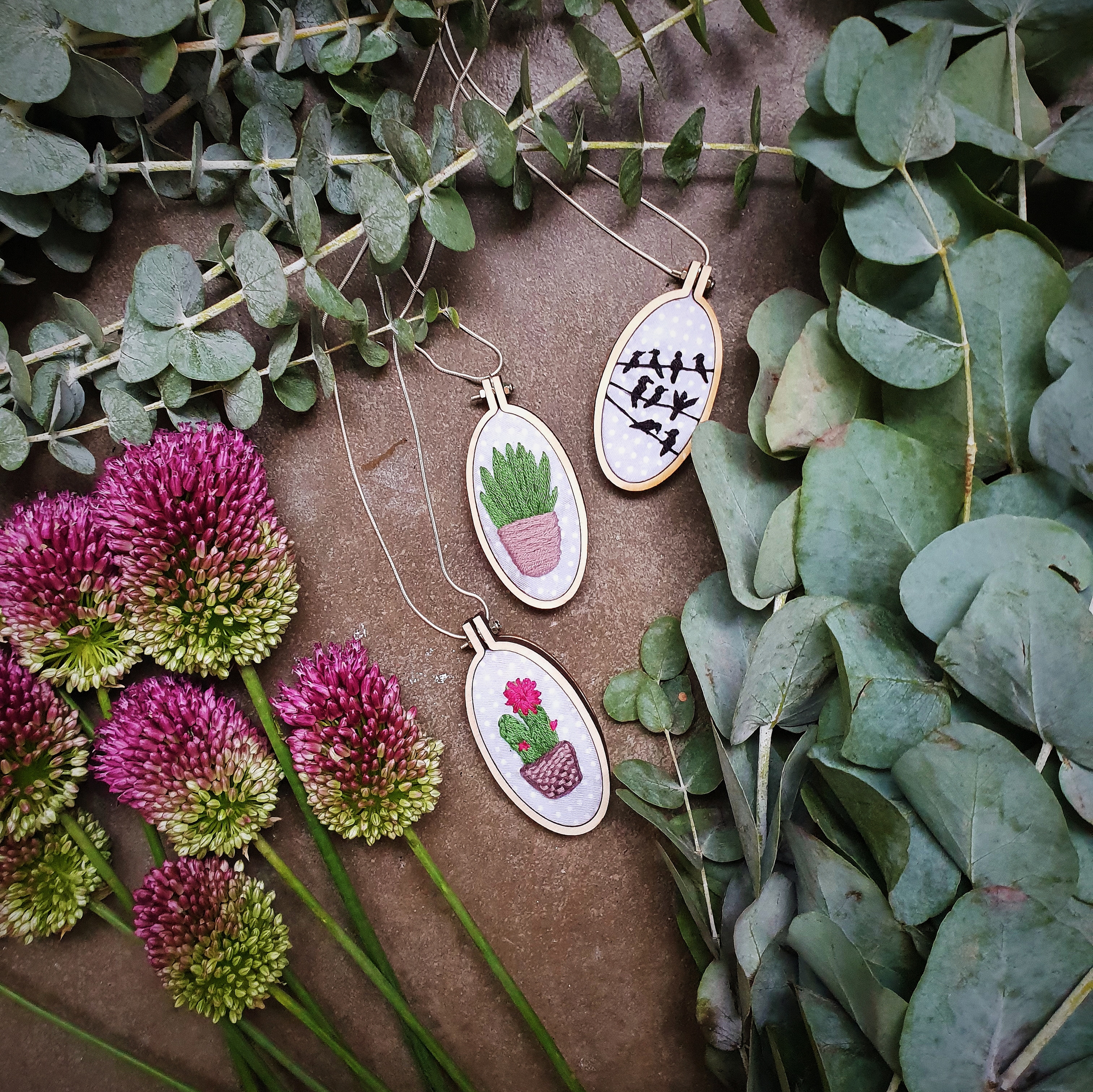 Flatlay photography featuring green and pink flowers surrounding three embroidered necklace