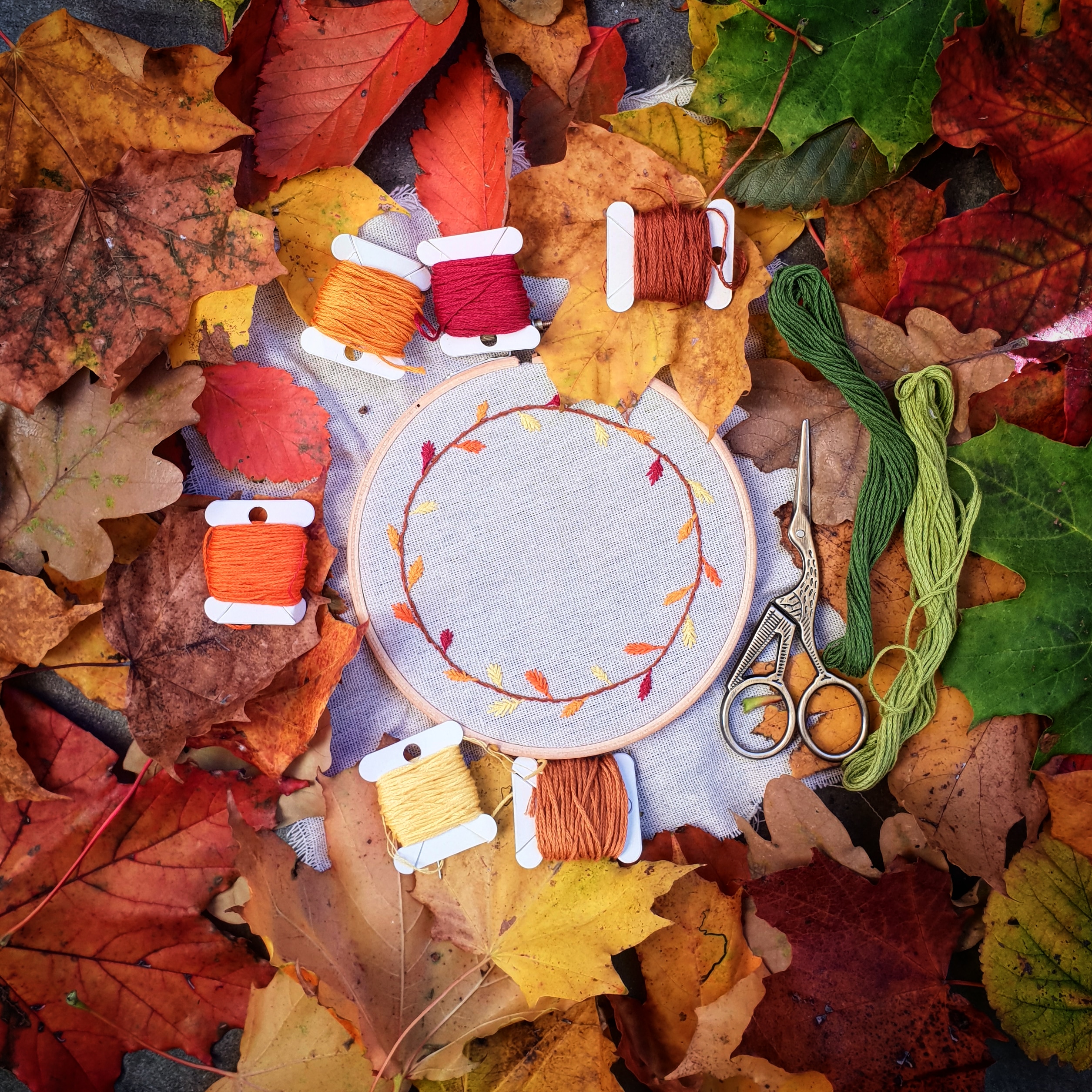 Embroidery of wreath in autumn colors surrounded by autumn leaves